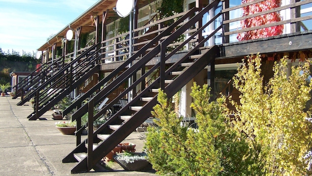 A row of wooden buildings with external staircases, potted plants, and hanging lights. - Mobile Home im Ferienpark mit Seezugang (Dabel)