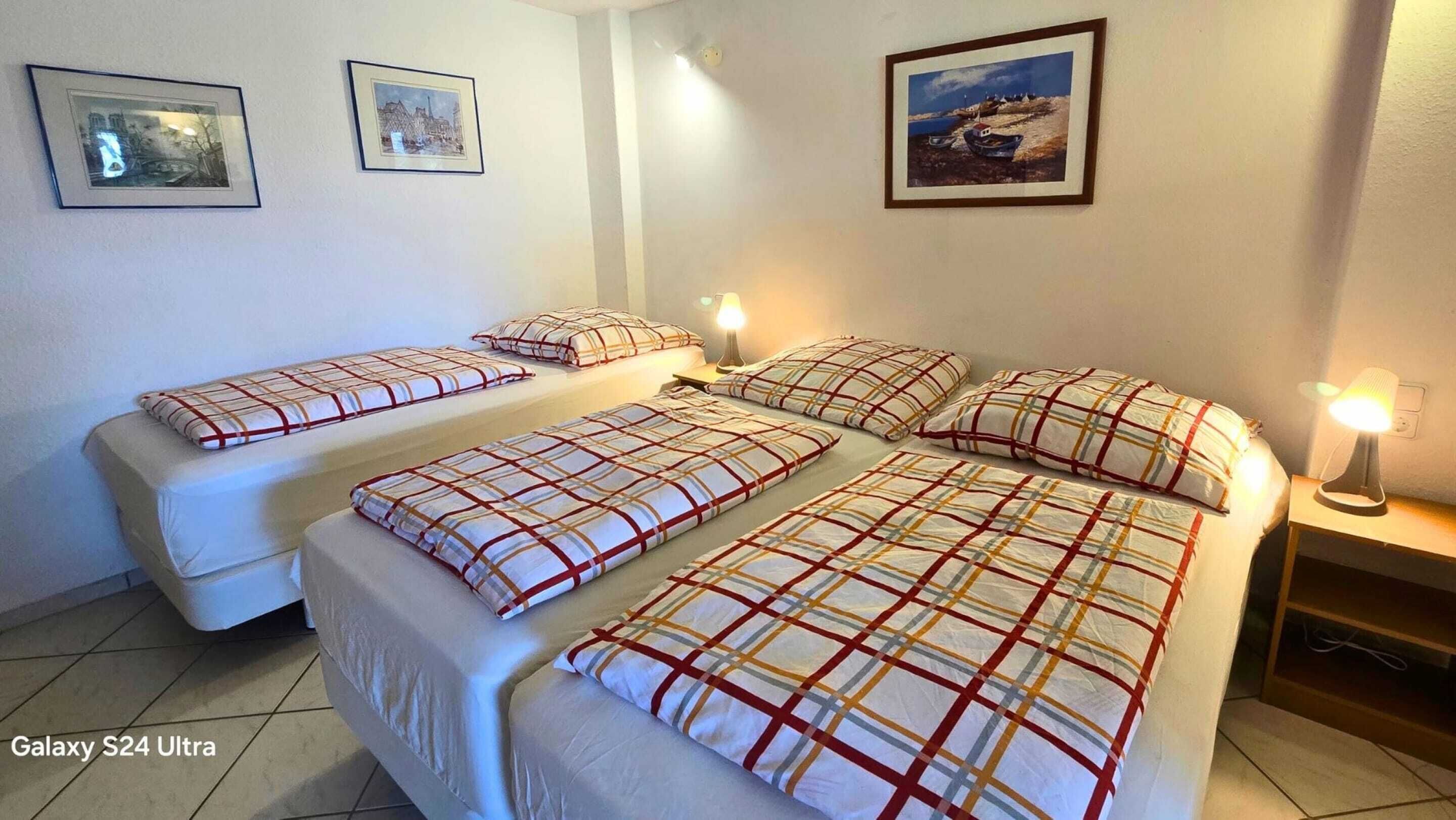 Habitación de hotel con tres camas, una mesita de noche y lámparas de pared.