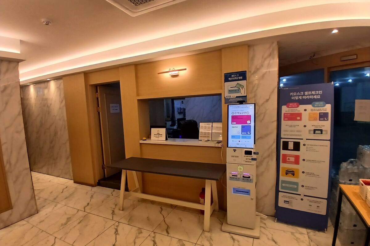 A hotel reception area with a digital kiosk, a bench, and a wall-mounted information board.