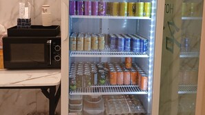 A UNICOOLA vending machine stocked with beverages and snacks, a microwave, and a small table with a tissue box. - Incheon Business Hotel Myung-Jak (Incheon)