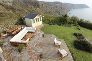 Um pátio com deck de madeira, um sofá embutido e um pequeno galpão com telhado preto.