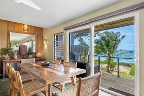 Ein Essbereich mit Holztisch, Korbstühlen, einem großen Spiegel und Blick auf das Meer durch eine Schiebetür.