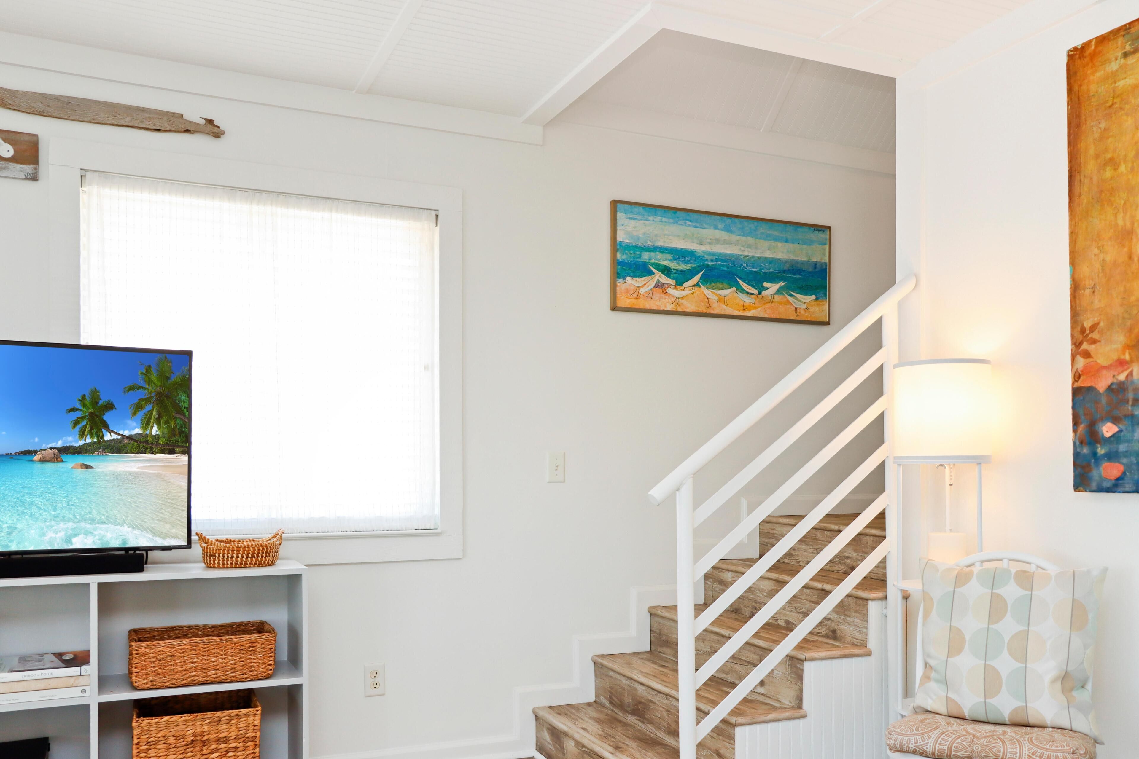 Un escalier avec des rampes blanches, un téléviseur posé sur une étagère blanche et un tableau représentant une scène de plage.