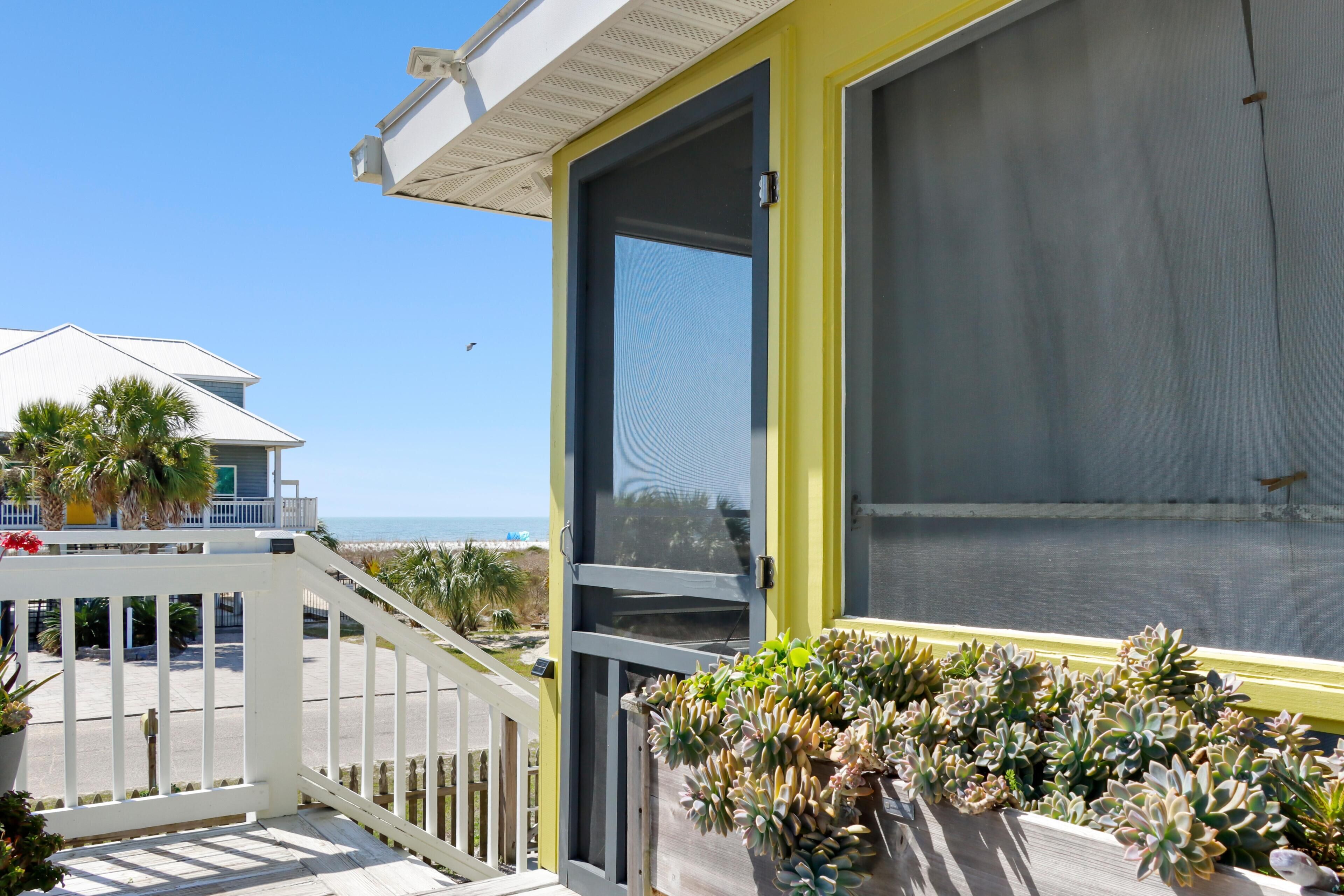A balcony with a view of the ocean, a white railing, and a potted plant arrangement.