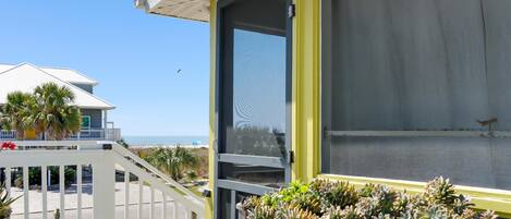 A balcony with a view of the ocean, a white railing, and a potted plant arrangement.