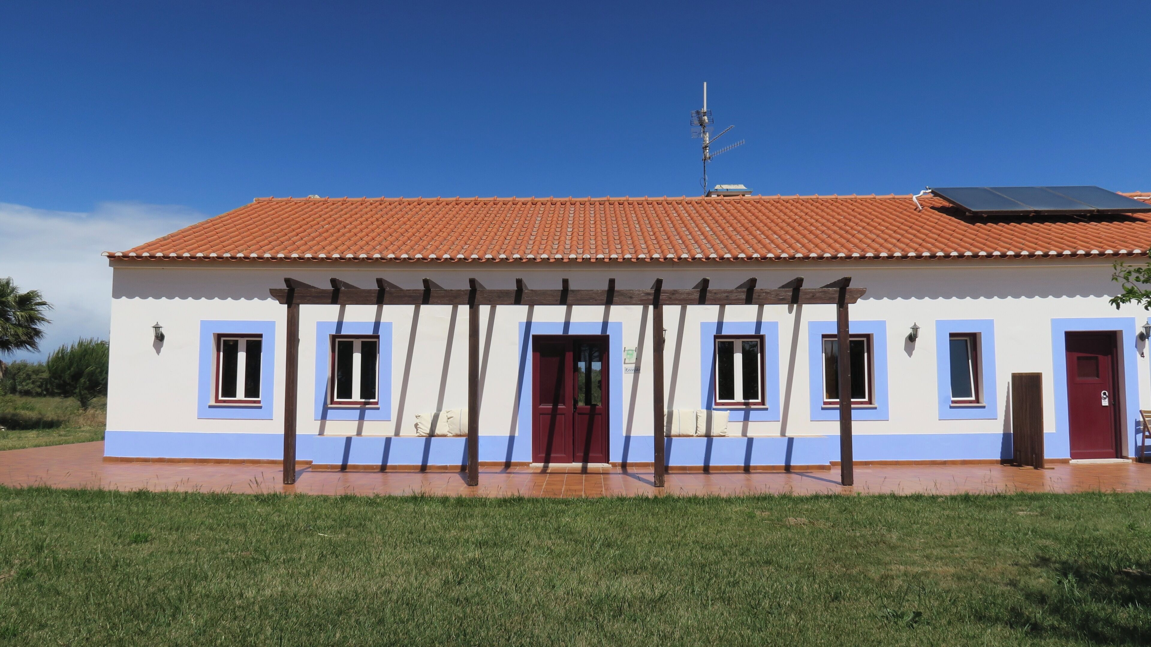 Un edificio con techo de tejas, varias ventanas, una puerta y un panel solar.