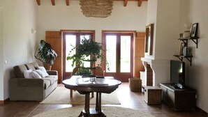 A living room with a sofa, a round table, a hanging light fixture, and a television. - Monte da Estrada - Turismo Rural (Zambujeira do Mar)