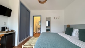A bedroom with a bed, a TV, a desk with a coffee maker, and a bathroom visible through an open door. - Monte da Estrada - Turismo Rural (Zambujeira do Mar)
