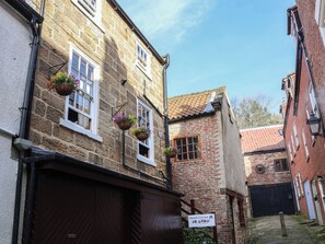 A narrow street with stone buildings, a sign for Bishop's Cottage, and hanging flower baskets. - Bishop's Cottage (Whitby)