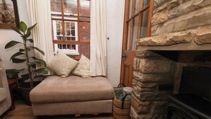 A cozy living room with a stone fireplace, a cushioned bench, a potted plant, and a window with curtains. - Bishop's Cottage (Whitby)