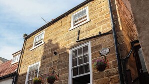 A stone building with multiple windows, some with flower baskets, and a sign indicating 'Bishops Cottage.' - Bishop's Cottage (Whitby)
