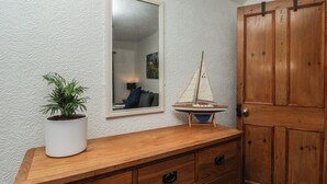 A wooden dresser with drawers, a potted plant, a mirror, and a model sailboat. - Bishop's Cottage (Whitby)