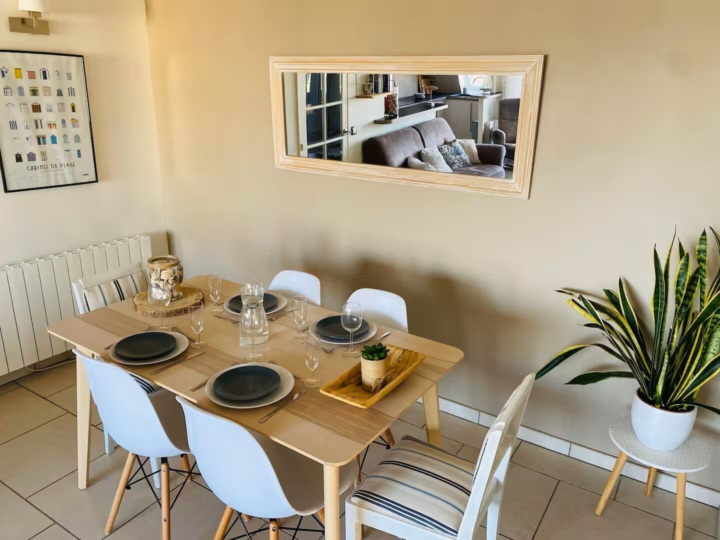 Un coin repas avec une table dressée pour quatre personnes, des chaises, une plante en pot et un miroir au mur.