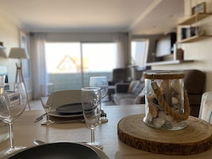 Ein Esstisch mit Geschirr, Gläsern und Besteck, ein Glas mit Muscheln und ein Holz-Untersetzer.