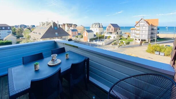 En takterrass med ett bord och stolar, med utsikt över en kuststad med dess byggnader och havet.