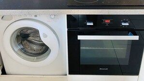 Ett kompakt kök med en inbyggd tvättmaskin, ugn och en köksfläkt med glasskärm.