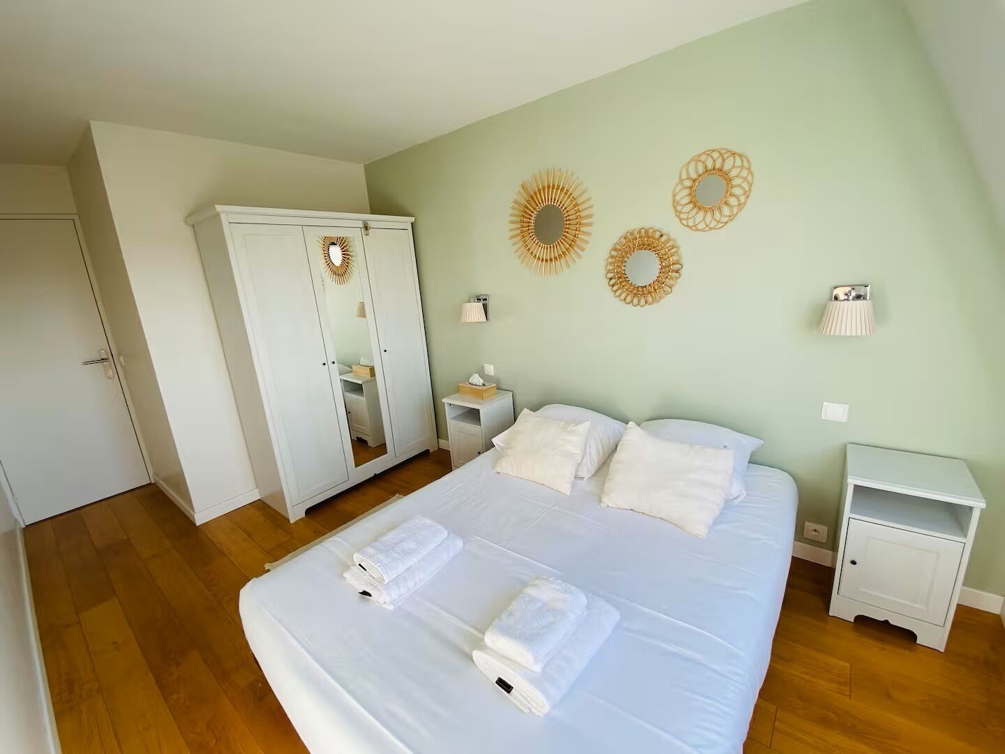 A bedroom with a bed, white wardrobe, bedside tables, and decorative wall mirrors.