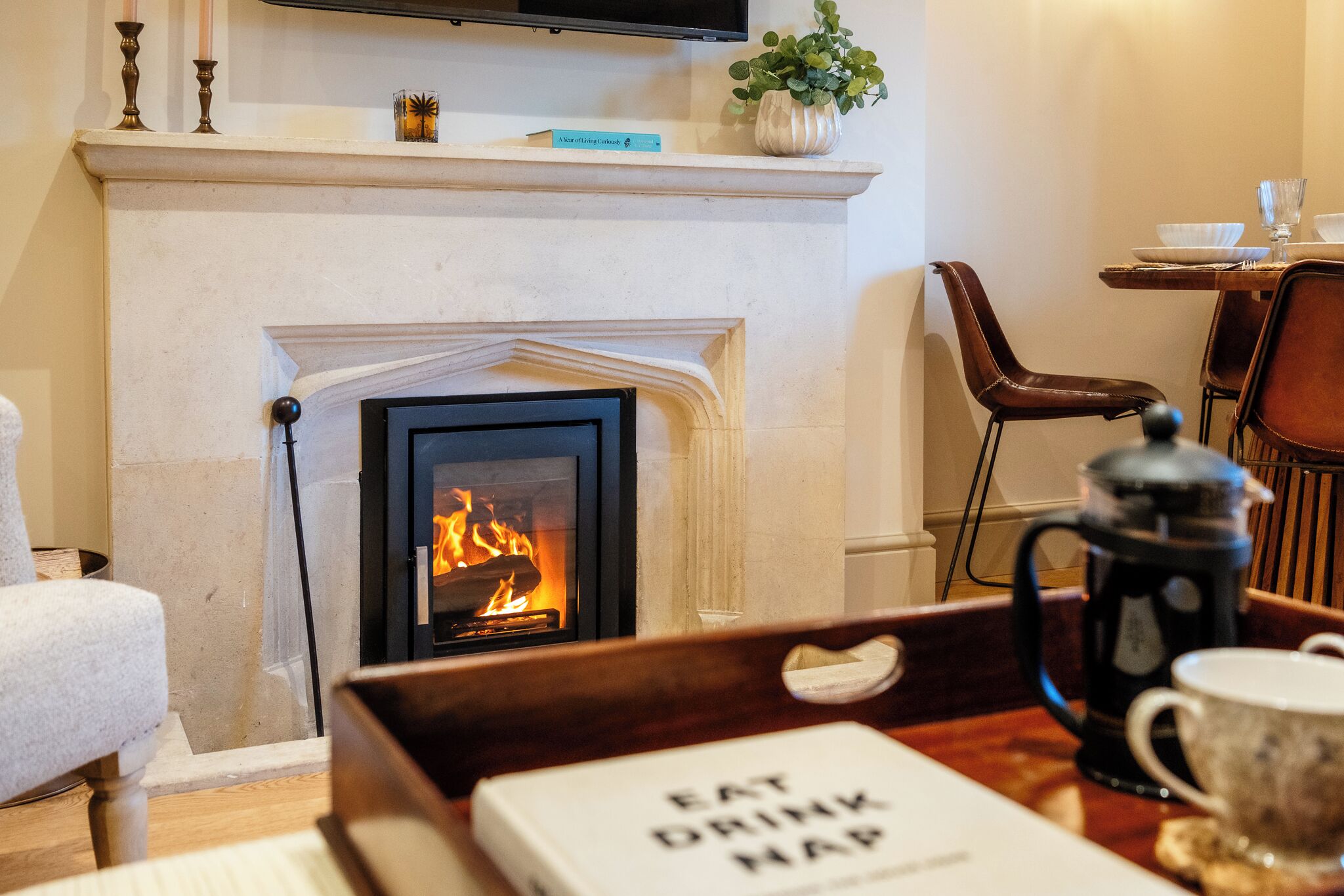 A cozy room with a fireplace, a dining table with chairs, and a tray with a book titled 'EAT DRINK MAP'.