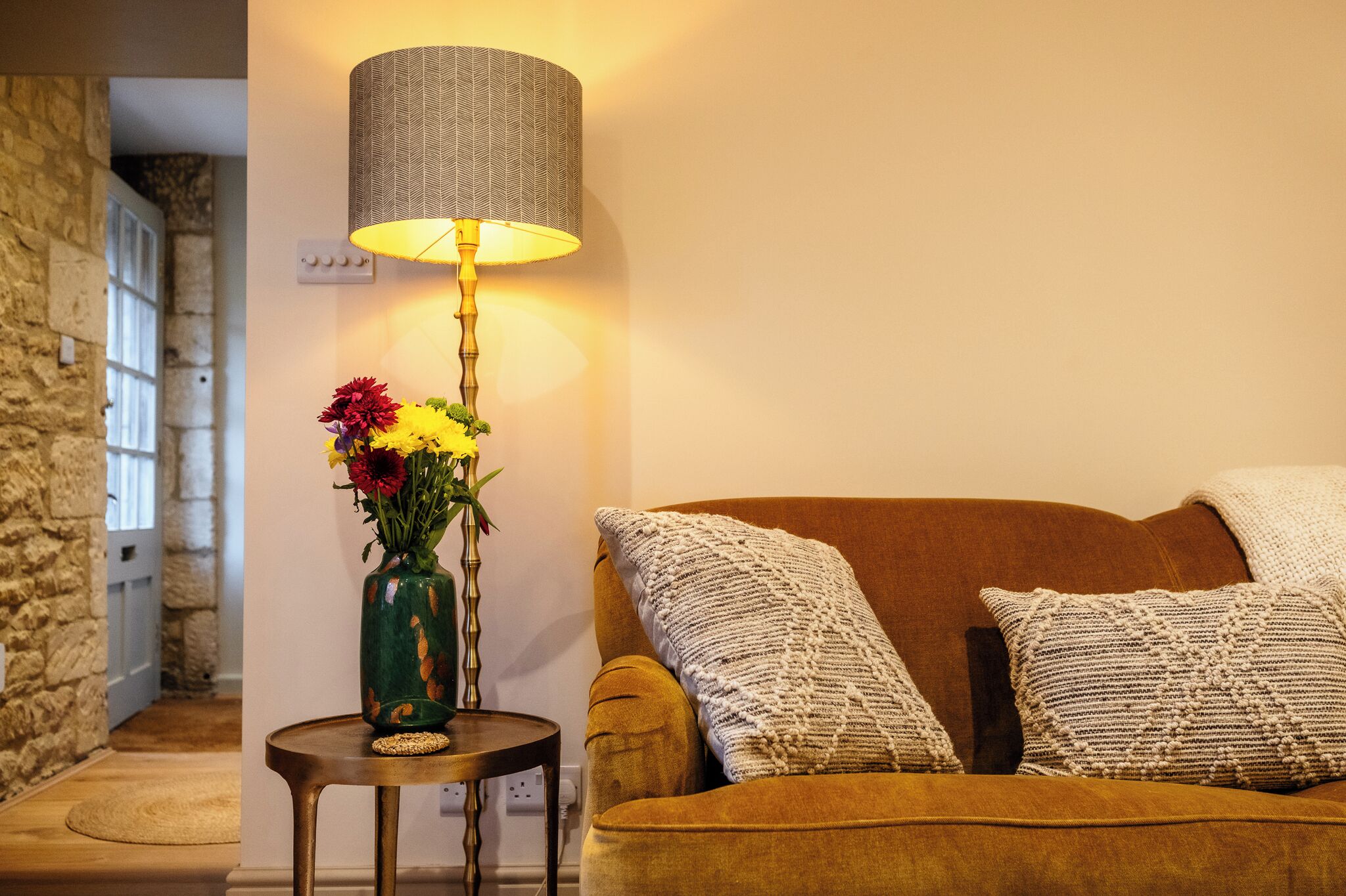 Ein Zimmer mit einem braunen Sofa, einer Lampe und einer Blumenvase.