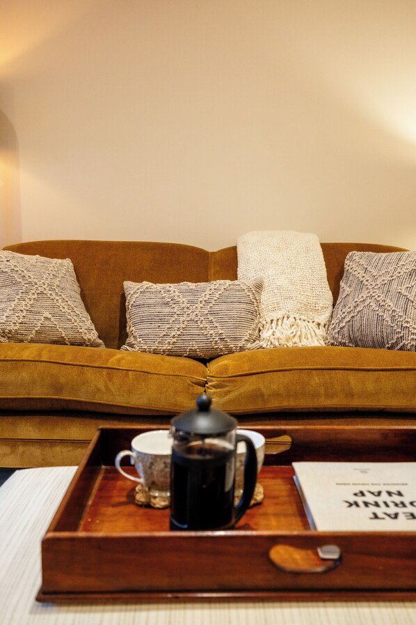 Un canapé marron agrémenté de coussins tricotés, un plateau avec une cafetière, une tasse et un livre.