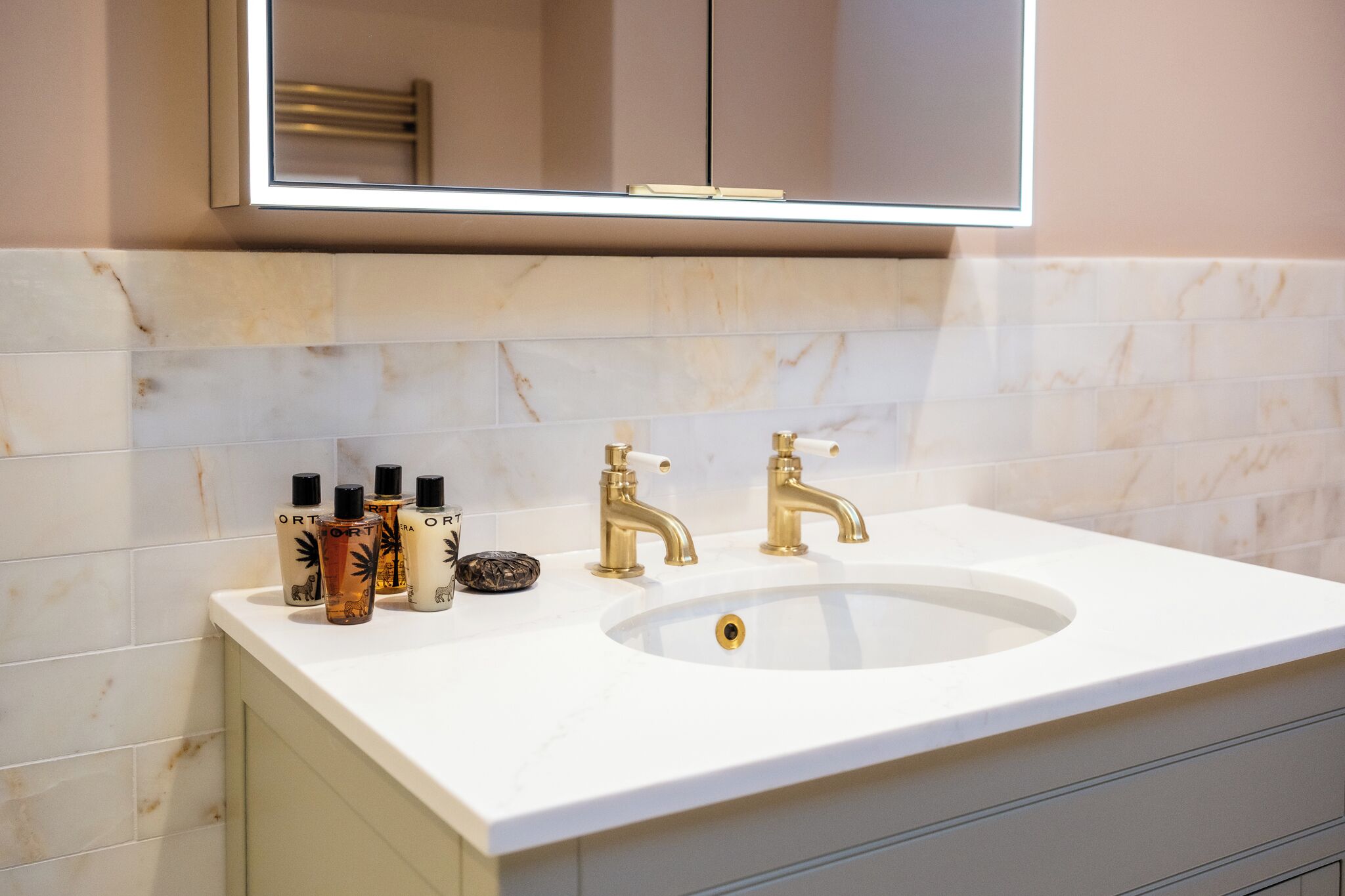 A bathroom with a white marble sink, gold faucets, and toiletries on the counter.