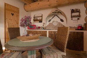 A rustic kitchen with wooden cabinets, a round table, wicker chairs, and a decorative wall with a heart-shaped cutout. - Comfortable Apartment Very Close to the Beach (gmina Będzino)