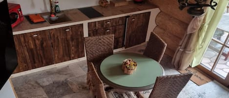 A kitchen with wooden cabinets, a round table with chairs, a kettle, and a small window with curtains.