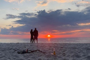 A beach scene with a sunset, two silhouetted figures, and a bottle on the sand. - Comfortable Apartment Very Close to the Beach (gmina Będzino)