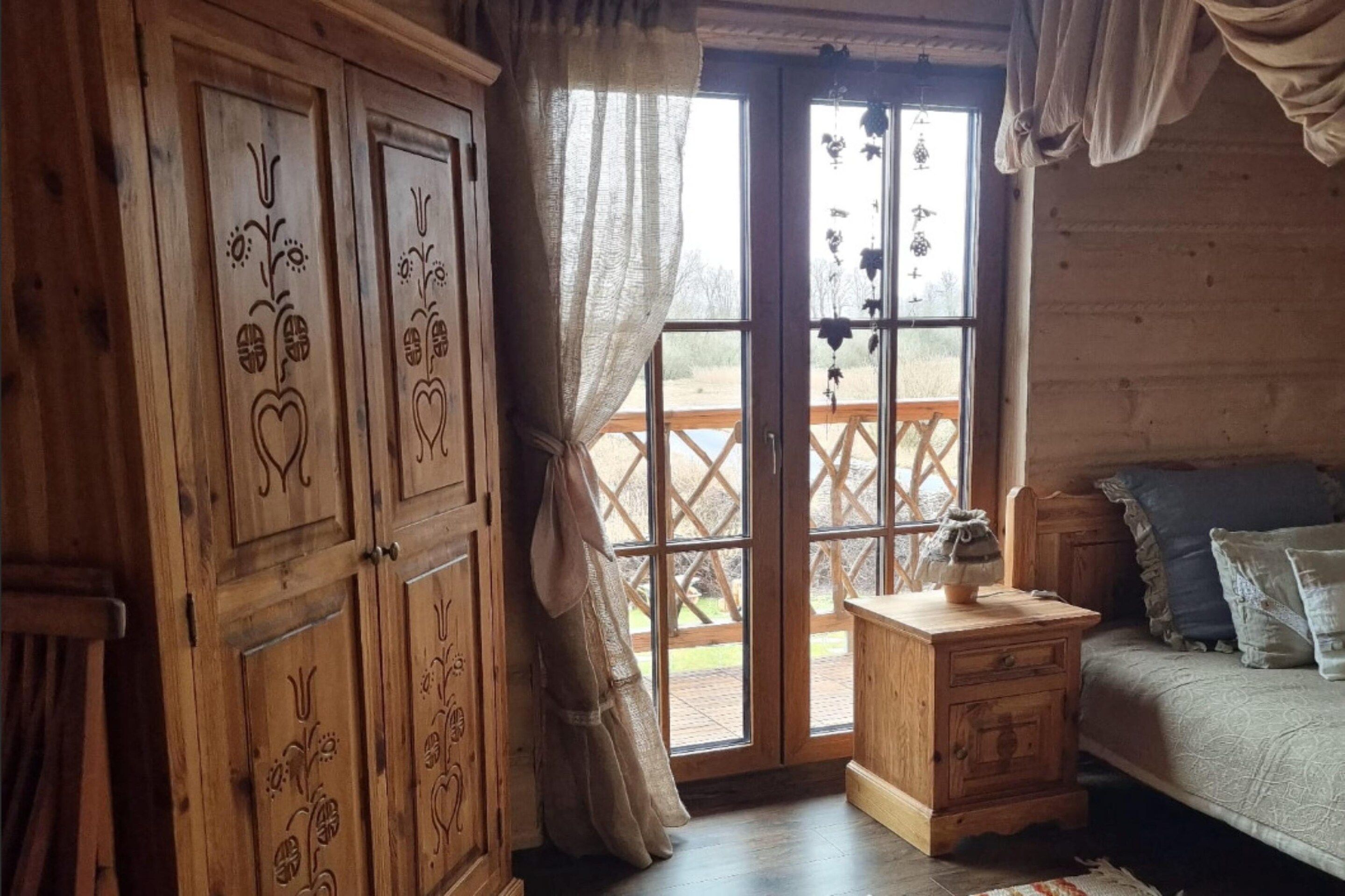 A wooden room with a bed, a nightstand, and a window with curtains.