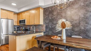 A modern kitchen with wooden cabinets, a stainless steel refrigerator, a microwave, and a dining area with a wooden table and chairs. - Mountain Chic | 2BR Family Escape | Hot Tub + Pool (Canmore)