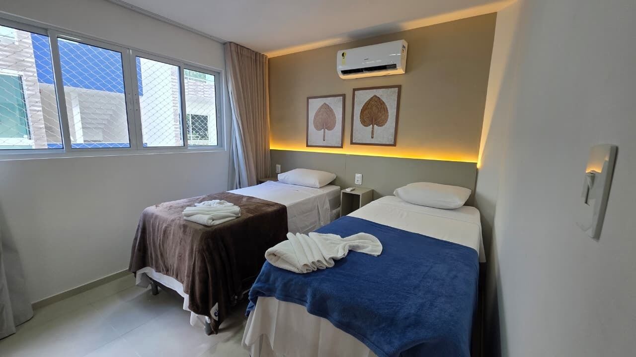 Habitación de hotel con dos camas, una ventana, aire acondicionado y una obra de arte en la pared.