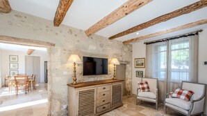 Una camera rustica con travi a vista in legno, un muro in pietra, un mobile contenitore in legno con cassetti, una televisione e due poltrone con cuscini a quadretti.