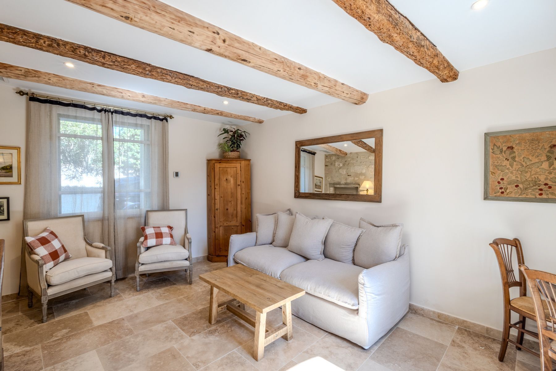 A living room with a white sofa, two armchairs, a wooden coffee table, and exposed wooden beams on the ceiling.
