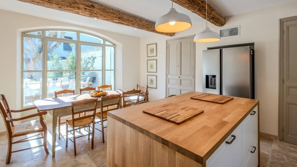 Cucina con isola grande, sedie in legno, tavolo da pranzo e vista attraverso ampie finestre.