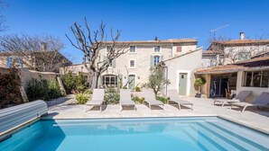 Una piscina con lettini, un edificio in pietra e un albero al centro.