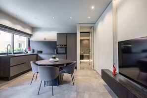 Une cuisine moderne avec un coin repas, un grand téléviseur et une vue sur l’extérieur.