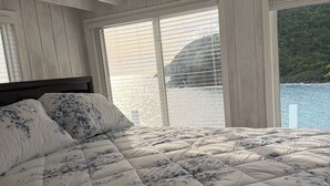 Quarto com uma cama grande, vigas de madeira no teto e vista para a água.