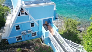 Um edifício azul com painéis solares, escadas e vista para o oceano.