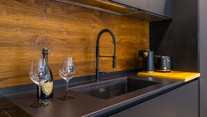 Une cuisine moderne avec un pare-feu en bois, un évier en acier inoxydable, un robinet noir, une bouteille de vin et un verre.