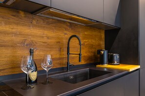 Een moderne keuken met een houten achterwand, een roestvrijstalen spoelbak, een zwarte kraan, een fles wijn en een glas.