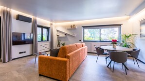 Un salon moderne comprenant un canapé, un téléviseur, une table à manger avec des chaises et une fenêtre donnant sur un paysage verdoyant.