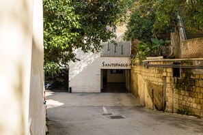 Een smalle steeg die leidt naar een gebouw met de naam 'SANTOPAULO', met aan één kant een bakstenen muur en aan de andere kant een witte muur.