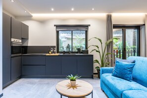 Een moderne keuken met donkere kasten, een centraal eiland en een zithoek met een blauwe bank en een ronde tafel.