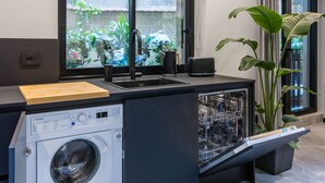 A modern kitchen with a built-in washer and dryer, a large window with a view of greenery, and a potted plant. - Santopaolo Boutique Apartment - 4 (Naples)