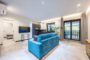 Een moderne woonkamer met een blauwe bank, een keukenhoek en een balkon met gordijnen.