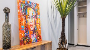 A hallway with a wooden console table, a colorful painting, a tall plant, and a door leading to a bathroom. - Santopaolo Boutique Apartment - 4 (Naples)