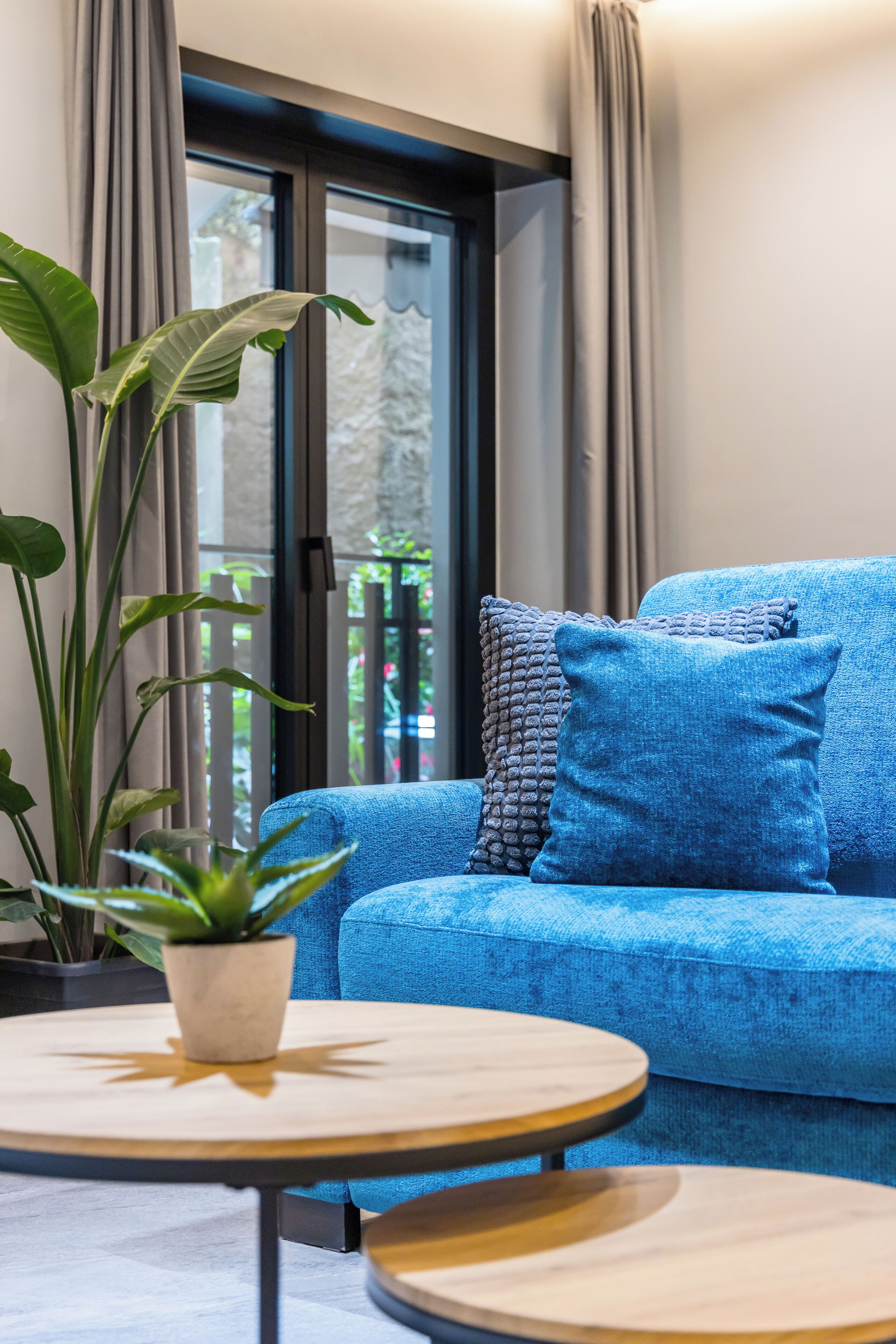Ein blaues Sofa mit einem Blumentopf und einem runden Tisch in einem Zimmer mit Blick durch eine Glastür.