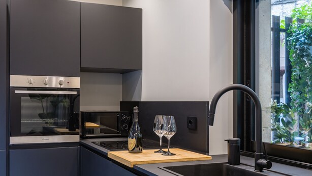 A modern kitchen with dark cabinetry, a built-in oven, a microwave, a black faucet, and a window with a view of greenery. - Santopaolo Boutique Apartment - 4 (Naples)