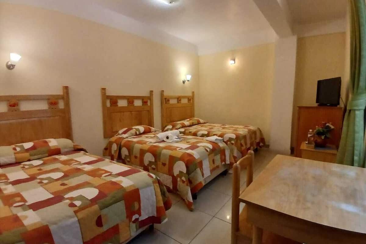 A hotel room with two beds, a wooden headboard, a small table, and a television on a stand.
