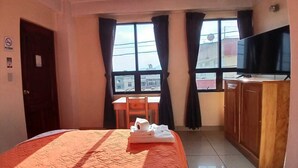 A hotel room with a bed, a desk, a chair, a television, and a window with curtains. - HOTEL Y RESTAURANTE MAYALAND (Quetzaltenango)